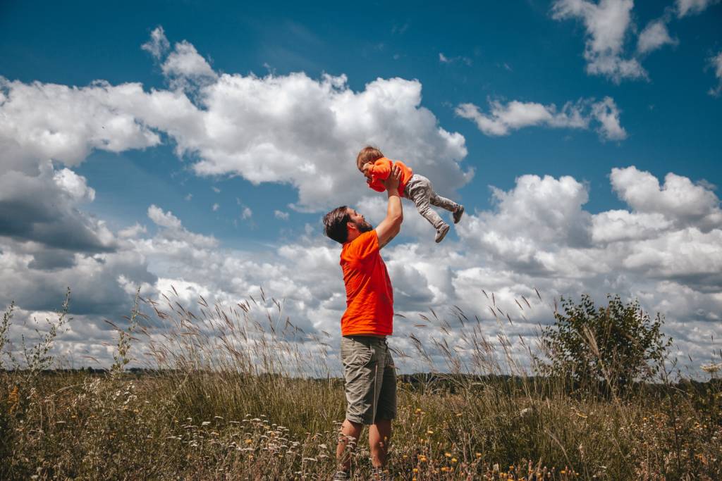 dad holding daughter up in the air in a field
