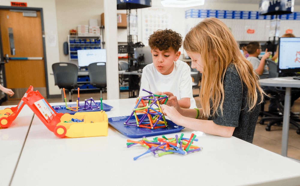 two children work together to build a structure out of magnetic building toys in a smartlab classroom setting