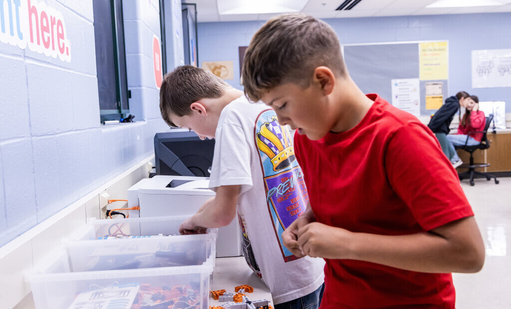 In a classroom, two boys are engaged in a project, focused on their work with books and supplies around them.