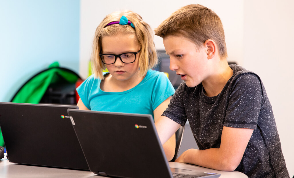a boy and a girl looking at their laptops together