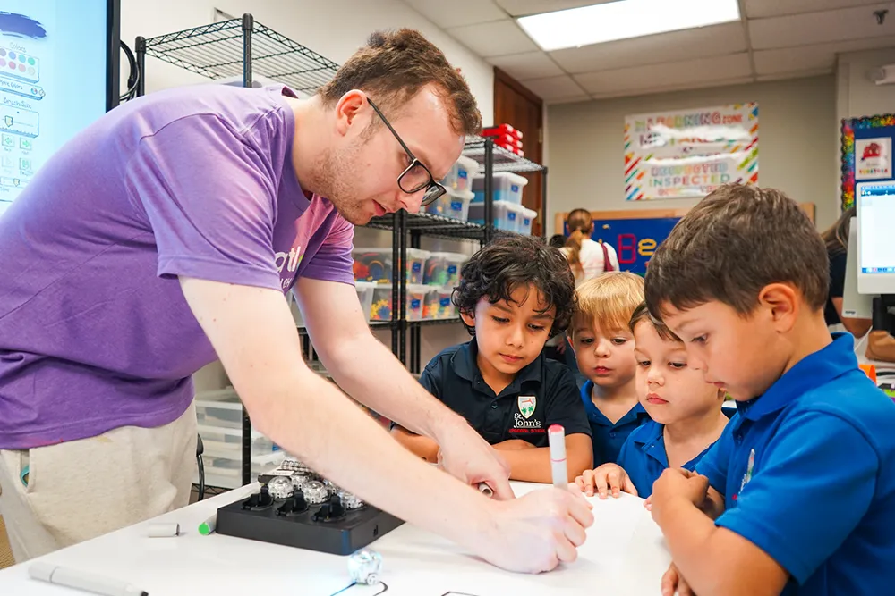 An adult instructor in a purple shirt demonstrates a hands-on activity to four young children.