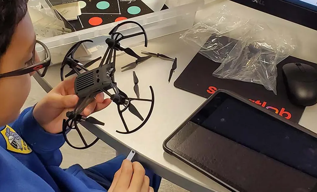 Person holding a small black quadcopter drone with propeller guards on a table.