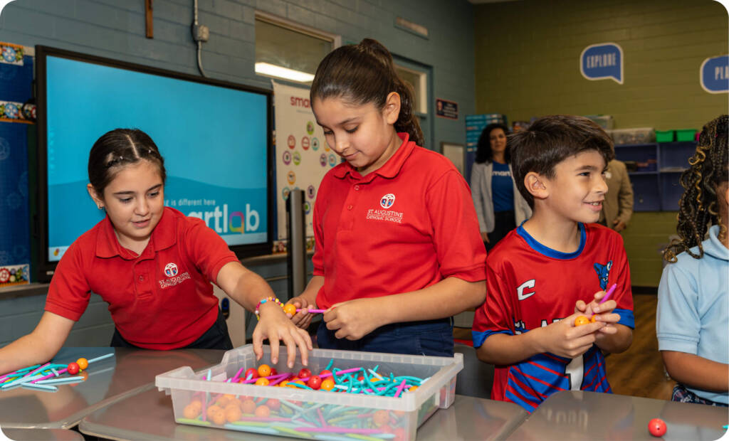 three elementary school kids play with STEM project materials in a classroom setting