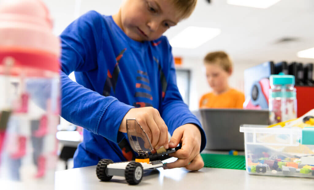 a school aged boy in a blue shirt plays with a car-making kit in a smart lab classroom