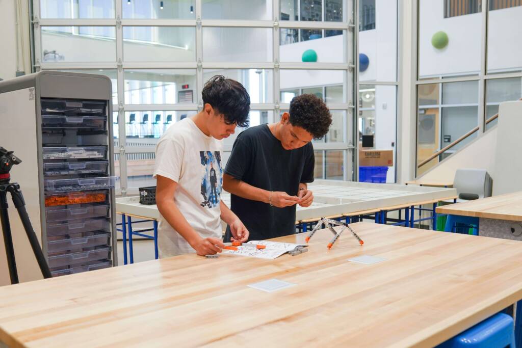 Two students building a VEX robotics structure together at a workbench in a STEM classroom
